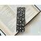 this floral bookmark has a black background. white and purple flowers, purple leaves, and white, green, and purple polka dots