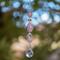 Large oval rose quartz bead flanked by Austrian crystal and two smaller round rose quartz beads, hanging vertically from a tree, anchored by round crystal prism