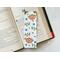the sloth bookmark has a white background with two sloths hanging from the branches, stems of leaves, blue flowers and leaves all over the bookmark