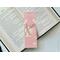 This pink Christmas bookmark has a pink background. There is a deer in the middle with Christmas lights hanging from the antlers. There is white Christmas ornaments hanging from the top with Christmas light on top of the bookmark.