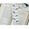 this bug book mark is on top of a open book with a pair of glasses in the back on a white table