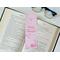 The romance bookmark is on top of an open book with a pair of glasses above and fairy lights on the right side on a white table