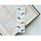 This moth bookmark has a white background with moths being beige and green. There are stars and moons all over the page saver