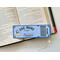 This bookmark looks like a ticket in color dark and light blue. In the center says 'One More Chapter Readers,' 'Lifetime Member' with a girl reading a book on the left and light blue flower. there are gold star boarders at each corner. Under the bar code the words 'ADMIT ONE'