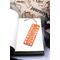 Front of bookmark  - orange background, hand painted paw print along sides, various dot art designs top, middle & bottom.  Jute rope tassel