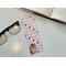 this Valentines Day bookmark is on a white table with an open book in the top right, and on the left is a pair of glasses and fairy light