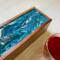 Close up of the blue, periwinkle and green design with white ribbons and bubbles on the top of this tea box for organizing tea bags.