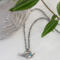 Sterling silver bird necklace with turquoise, on a white surface with green leaves and a decorative bowl.
