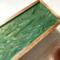 An up close look at the green and gold design that is finished in glossy resin atop this mango wood tea organizer.