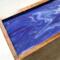 A close up of the top of this mango wood tea box shows ribbons of various shades of rich purple and white forming a pleasing design.  The glossy finish makes the colors even richer and adds interest and luxury to your home decor.