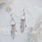  Pair of 925 sterling silver fringe dangle earrings displayed on a textured white surface with flowers and crystals.
