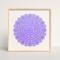 Leaning against a wall and framed in a blond wood, square frame, is the purple, round amulet.