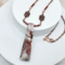 Handmade necklace with jasper pendant, garnet beads, and copper chain on a marble background.