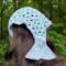 A woman with dark brown hair wearing a mermaid tail shaped crochet hair bandana that has light blue scales with light purple outlines.
