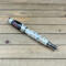 White fiberglass rollerball pen with custom bent watch parts. 