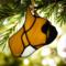 French Bulldog Stained Glass ornament made of tan colored glass, hanging on from a Christmas tree branch with white lights in the background.