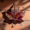 Sugar Male Leaf stained glass ornament hanging on a rustic barn wall wall. Made of a glass that has red, orange and yellow swirled within it, giving the look of a real sugar maple leaf.