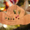 Handmade wooden Christmas tree ornament shaped like a cowboy hat, featuring a sprig of holly tucked into the hat band, star-shaped leaf cutouts, and round berry accents.