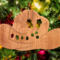 Handmade wooden Christmas tree ornament shaped like a cowboy hat, featuring a sprig of holly tucked into the hat band, star-shaped leaf cutouts, and round berry accents.