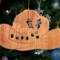 Handmade wooden Christmas tree ornament shaped like a cowboy hat, featuring a sprig of holly tucked into the hat band, star-shaped leaf cutouts, and round berry accents.