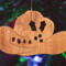 Handmade wooden Christmas tree ornament shaped like a cowboy hat, featuring a sprig of holly tucked into the hat band, star-shaped leaf cutouts, and round berry accents.