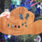 Handmade wooden Christmas tree ornament shaped like a cowboy hat, featuring a sprig of holly tucked into the hat band, star-shaped leaf cutouts, and round berry accents.