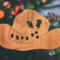 Handmade wooden Christmas tree ornament shaped like a cowboy hat, featuring a sprig of holly tucked into the hat band, star-shaped leaf cutouts, and round berry accents.