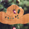 Handmade wooden Christmas tree ornament shaped like a cowboy hat, featuring a sprig of holly tucked into the hat band, star-shaped leaf cutouts, and round berry accents.