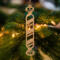 Handmade wooden Christmas tree ornament shaped like a peppermint stick with diagonal stripes, crafted from light-colored wood with flared decorative ends.