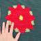 A close up of one of the red poinsettias on either end of the table runner. The maker's hand is in the photo to the left to show size. 