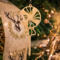 A handcrafted wooden Christmas tree ornament shaped like a lollipop, featuring intricate cut-out spiral patterns on the circular top and a simple stick base. The ornament is light brown with a smooth finish.