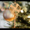 A handcrafted wooden Christmas tree ornament shaped like a lollipop, featuring intricate cut-out spiral patterns on the circular top and a simple stick base. The ornament is light brown with a smooth finish.