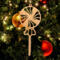 A handcrafted wooden Christmas tree ornament shaped like a lollipop, featuring intricate cut-out spiral patterns on the circular top and a simple stick base. The ornament is light brown with a smooth finish.