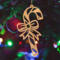 Handmade wooden Christmas tree ornament shaped like a curved candy cane with intricate stripe cutouts, accented by a delicate bow and crafted from natural light colored wood tones.