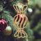 A handmade wooden Christmas tree ornament shaped like a wrapped hard candy, featuring a bulbous center with swirling stripes and twisted wrapper ends, crafted from light-toned wood using a scroll saw.