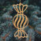 A handmade wooden Christmas tree ornament shaped like a wrapped hard candy, featuring a bulbous center with swirling stripes and twisted wrapper ends, crafted from light-toned wood using a scroll saw.