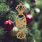 A handcrafted wooden Christmas tree ornament shaped like a wrapped candy, featuring intricate Victorian fretwork with twisted ends and a diagonal swirling stripe in the center.
