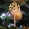 A handmade Christmas tree ornament crafted from light brown maple hardwood plywood, shaped like a lollipop with a round head featuring intricate spiral cutouts and a long stick handle, suspended from a small metal hook.