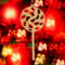A handmade Christmas tree ornament crafted from light brown maple hardwood plywood, shaped like a lollipop with a round head featuring intricate spiral cutouts and a long stick handle, suspended from a small metal hook.