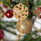 A handmade Christmas tree ornament crafted from light brown maple hardwood plywood, shaped like a lollipop with a round head featuring intricate spiral cutouts and a long stick handle, suspended from a small metal hook.