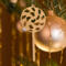 A handmade Christmas tree ornament crafted from light brown maple hardwood plywood, shaped like a lollipop with a round head featuring intricate spiral cutouts and a long stick handle, suspended from a small metal hook.