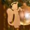 A handmade wooden Christmas ornament in the shape of a cheerful angel, featuring a halo, wings, and a raised arm ringing a bell, hand-cut from solid hardwood and finished with clear shellac.