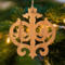Intricate Victorian-style fretwork Christmas tree ornament handcrafted from natural hardwood with visible wood grain, showcasing symmetrical curls, loops, and ornate cut-out designs.