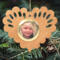 Wooden heart-shaped ornament with scalloped edges and an oak grain finish, featuring a removable round gold frame that holds a photo of a smiling blonde child.