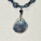 Closeup of ceramic shell pendant with blue-brown ridges attached to strand of sodalite beads and Czech crystals