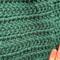 A close up of the green crochet stitches on the main scarf. The maker's fingers are in the photo for size context.