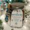 Handcrafted Hot Cocoa Jar decorated with blue ribbon and surrounded by blue and silver Christmas ornaments.