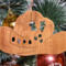 Handmade wooden Christmas tree ornament shaped like a cowboy hat, featuring a sprig of holly tucked into the hat band, hand cut holly leaf cutouts, and round berry accents.