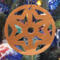 A handmade wooden Christmas tree ornament, circular in shape, crafted from light brown wood with a natural grain pattern. It features an intricate, symmetrical cutout design resembling a star or snowflake, with multiple pointed shapes radiating from a central hole. The ornament is attached to a small metal hook for hanging, showcasing its rustic and festive craftsmanship.