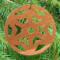 A handmade wooden Christmas tree ornament, circular in shape, crafted from light brown wood with a natural grain pattern. It features an intricate, symmetrical cutout design resembling a star or snowflake, with multiple pointed shapes radiating from a central hole. The ornament is attached to a small metal hook for hanging, showcasing its rustic and festive craftsmanship.